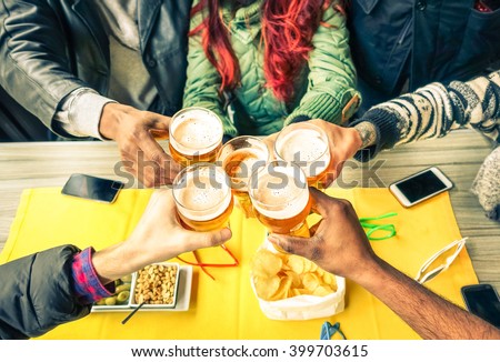 Group of friends cheers with beer cafe interior scene - Multiracial hands holding glasses of Pils in a toast to friendship and happiness -Teenager students gathering in restaurant -  Focus on glasses