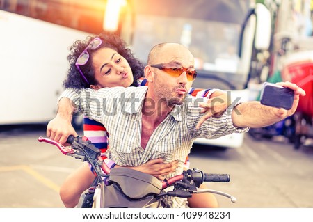 Couple of bikers taking selfie riding motorbike on urban road at sunset -  Cool man and beautiful girl on sport motorcycle with funny facial expression - Concept of dangerous drive - Focus on male