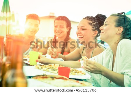 Friends having fun eating pizza at sunset on beach bar restaurant - Cheerful teenagers laughing at dinner party on summer vacation - Concept of joyful meal together Desaturated vintage filter look