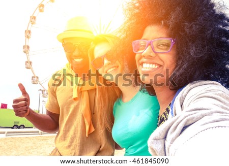 Afro hair girl taking selfie with best friends at ferris wheel at sunset - Happy multiracial group of students having fun with smartphone photo camera outside- Warm sun halo filter with vintage tones