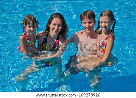 Happy family with two kids in swimming pool. Smiling parents and children on summer vacation swim and having fun. Family sport, active healthy holiday