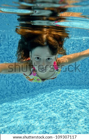 Happy smiling underwater child jumps to swimming pool, beautiful little girl swims and having fun. Kids sport on family summer vacation. Active holiday