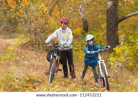 Happy family on bikes cycling outdoors, smiling active mother with kid on bicycles having fun, golden autumn in park. Family sport and healthy lifestyle