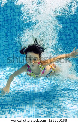 Happy smiling underwater child jumps to swimming pool, beautiful little girl swims and having fun. Kids sport on family summer vacation. Active healthy holiday