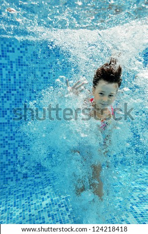 Happy smiling underwater child jumps to swimming pool, beautiful little girl swims and having fun. Kids sport on family summer vacation. Active holiday