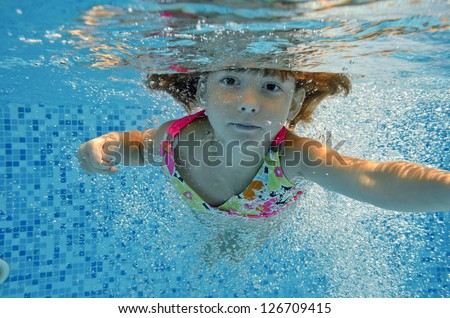 Underwater child jumps to swimming pool, beautiful little girl swims and having fun. Kids sport on family summer vacation. Active holiday
