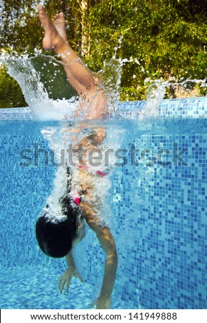 Active underwater child jumps to swimming pool, little girl swims and having fun. Kids sport on family summer vacation. Active holiday