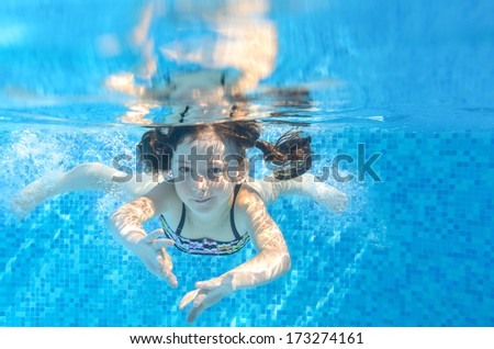 Happy active child swims underwater in pool, beautiful healthy girl swimming and having fun on family summer vacation, kids sport concept