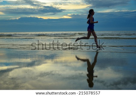 Silhouette of woman jogger running on sunset beach with reflection, fitness and healthy life concept