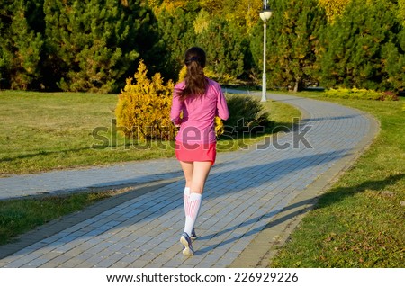 Woman running in autumn park, beautiful girl runner jogging outdoors, back view, training for marathon, exercising and fitness concept