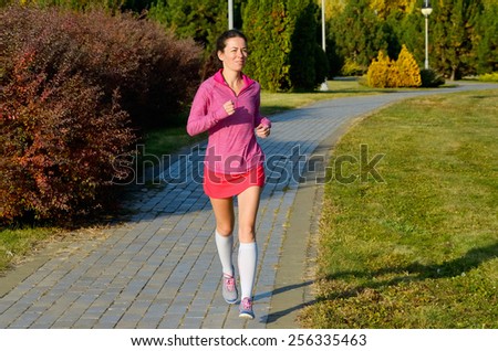Woman running in autumn park, beautiful girl runner jogging outdoors, training for marathon, exercising and fitness concept