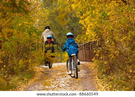 Family cycling outdoors, golden autumn in park. Father with kids on bicycles