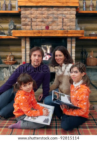Happy family having fun near fireplace in wooden house. Parents with kids reading books on winter weekend
