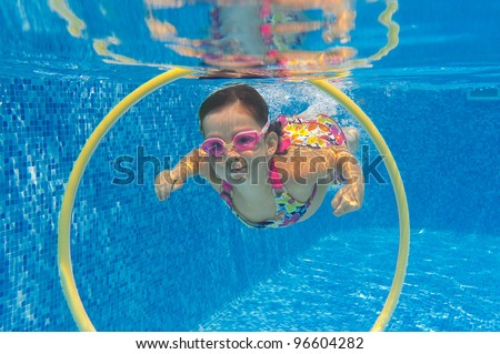 Happy child swims underwater in swimming pool. Smiling active girl in pool. Kids sport and fun