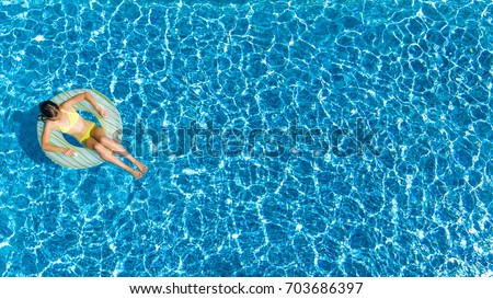Aerial top view of girl in swimming pool from above, kid swims on inflatable ring donut , child has fun in water on family vacation
