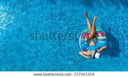 Aerial top view of beautiful girl in swimming pool from above, relax swim on inflatable ring donut and has fun in water on family vacation