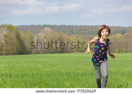 Happy active girl running on green field. Child and nature in spring, summer