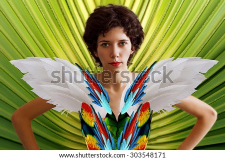 Young beautiful girl in the image of a parrot in a brightly colored feathers and wings. A woman in a tropical jungle. Fantastic image.