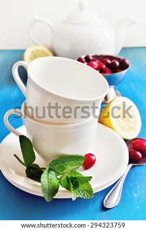 Tea with lemon, mint, and fresh cranberries on a blue background. Table setting for tea time, porcelain cups, table setting for tea time, selective focus