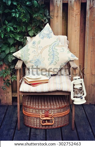 A cup of coffee on a chair on a terrace or a patio. Vintage objects, lamp, picnic basket, pillows, books. Toned image, selective focus.