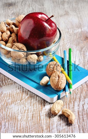 A bowl with snacks, nuts and apple, stationery, a notebook and pencils, back to school and learning concepts, selective focus