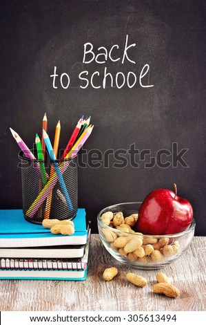 Chalk board, stationery, notebooks, color pencils, snack, nuts, apple, back to school and learning concepts, selective focus