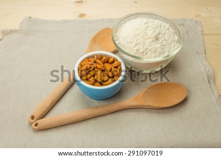 A blue ceramic bowl with almonds, a glass bowl with flour, wooden spoon and spatula