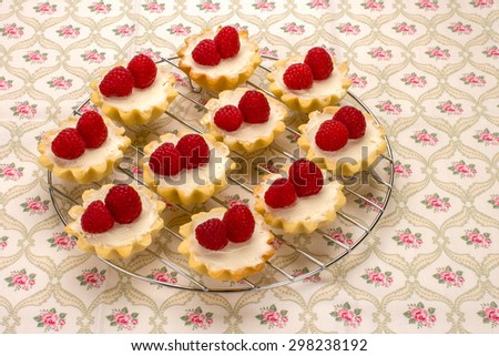 Homemade small cakes with cream cheese and fresh raspberries on a cotton napkin with a flower pattern