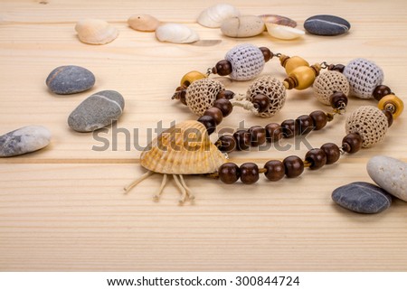 Handmade necklaces pendant from sea shells, beads knitted on the background light wooden boards and sea stones