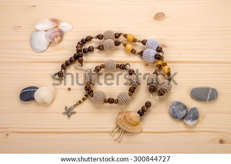 Handmade necklace and bangle with knitted beads, pendant from sea shells and starfish pendant on a wooden table with a sea pebbles
