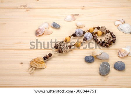 Necklaces handmade pendant from sea shells, beads knitted on the background light wooden boards and sea stones