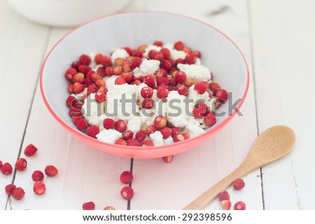 Cottage cheese with strawberries served in a bowl with red edges on a white wooden table