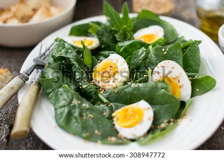 Salad with spinach, eggs and sesame seeds served with toasted white bread and olive oil on a white oval plate on wooden background