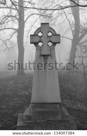 Celtic Cross in very foggy and spooky looking graveyard,