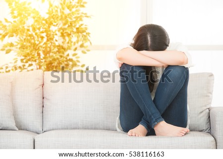 Sad depressed woman at home she is sitting on the couch. loneliness and sadness concept lifestyle and health concept. mixed race asian chinese model.
