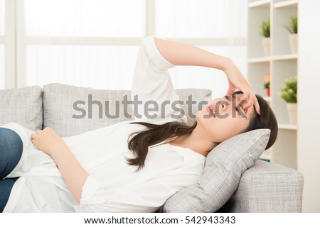Young woman with headache lying on couch at home. casual style indoor shoot. lifestyle and health concept mixed race asian chinese model.