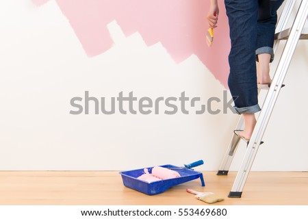Beautiful young woman standing on ladder doing wall painting. mixed race asian chinese female model