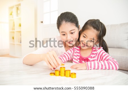 happy asian mother teach her daughter how to saving and calculate money everyday in the living room at home. family activity concept.