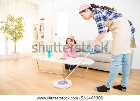 mum teaching daughter cleaning their home living room at weekend. A young woman and a little child girl dusting. family housework and household concept.