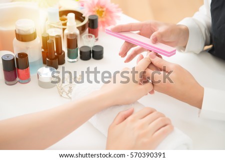 Hardware manicure in a beauty salon. asian chinese manicurist is applying nail file drill to manicure on female fingers. real salon spa background. beauty and fashion concept.