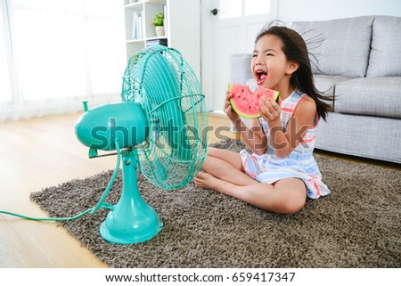 beautiful youth girl holding watermelon sitting in front of electric fan and blowing cool fan for eliminating summer hot.