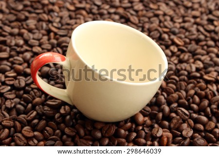 Closeup of dark roasted coffee beans and an empty  cup. Food and drink backdrop showing aromatic and beautiful coffee beans.