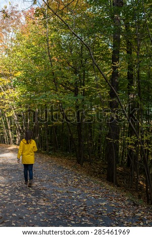girl with a yellow oilskin walking on way in a park in the middle of trees during indian summer
