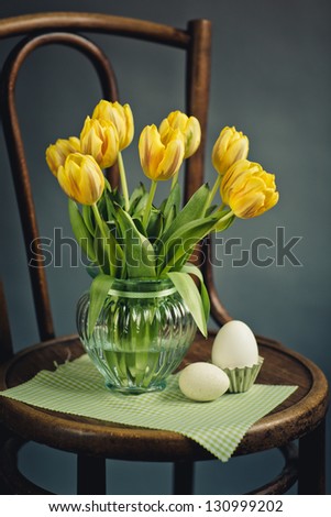 Beautiful bright yellow tulips in Still Life in Glass Vase on antique wooden Chair with fresh white Eggs