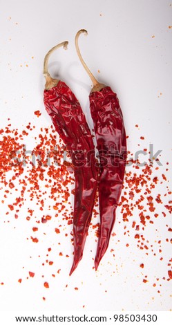 Two dried red hot chili peppers with flakes of grounded peppers