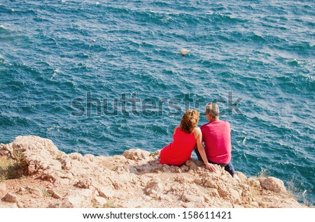 mature couple sitting close together on the beach gazing out to sea