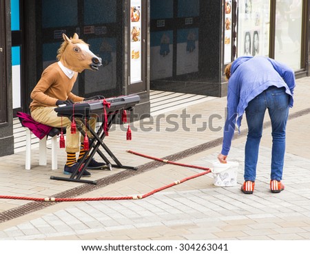 LEEDS, UK - 24 July 2015.  Man with a horses head playing the keyboard and busking for money.  Lady putting money into busker, begger, performer\'s hat