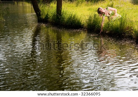 a happy woman sitting on the grass of the lakes coast, touching the water