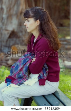 Middle aged brown haired woman sitting on a park bench collecting her thoughts