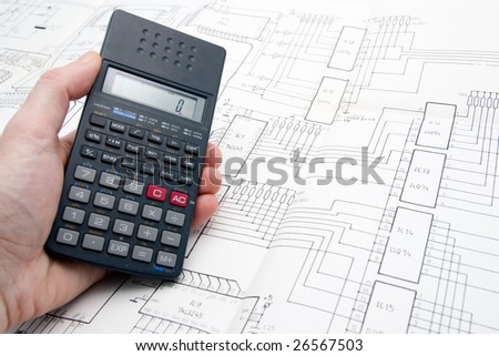 Engineer working on a project with a calculator on his hand and an schematic on the table